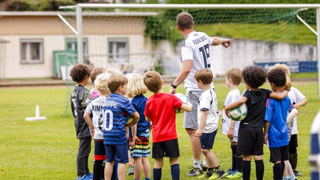 Ein ehrenamtlicher Trainer trainiert Kinder auf einem Fussballplatz