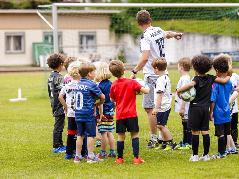 Ein ehrenamtlicher Trainer trainiert Kinder auf einem Fussballplatz