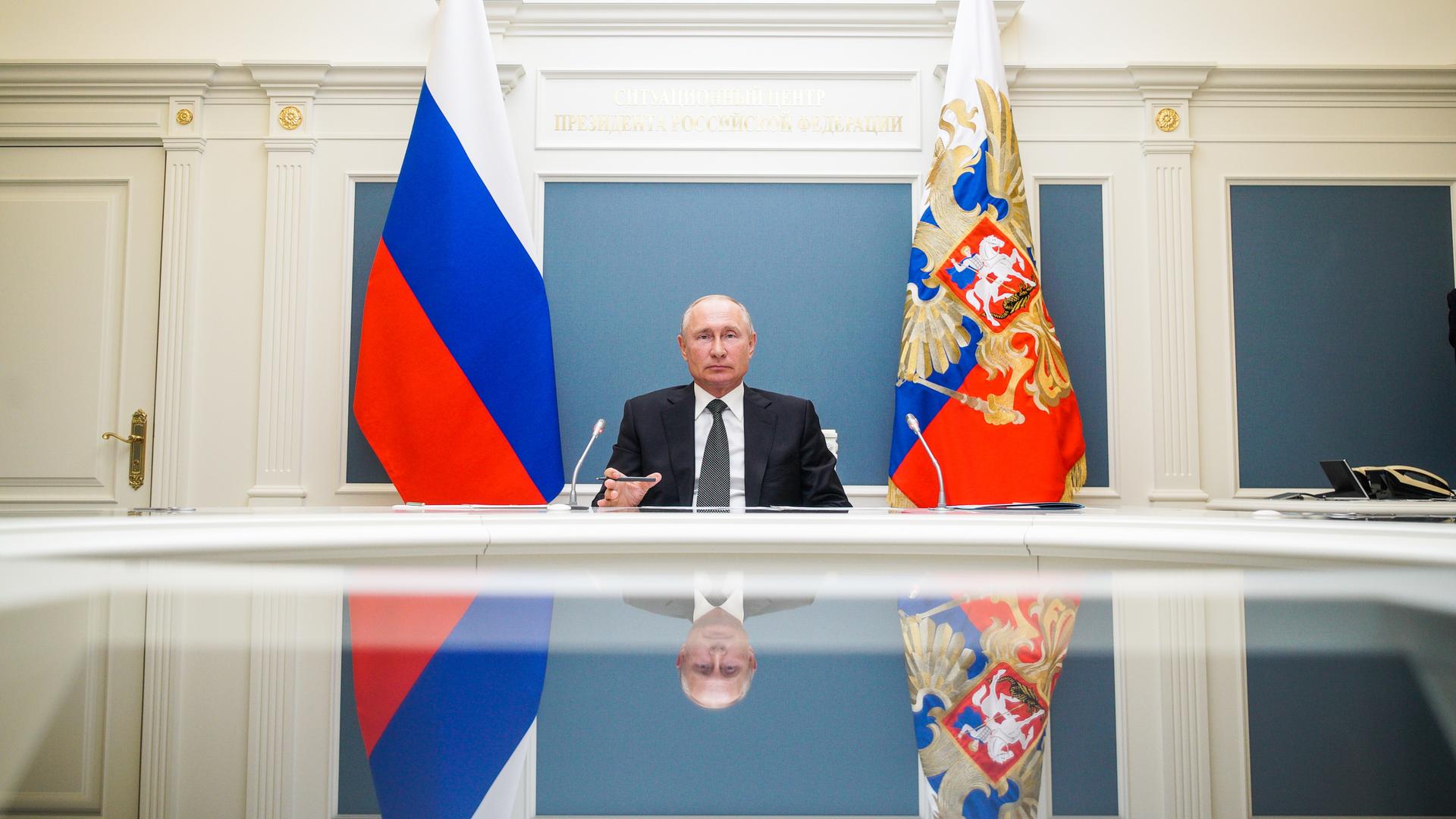 Russlands Präsident Wladimir Putin an einem Schreibtisch, hinter ihm Fahnen