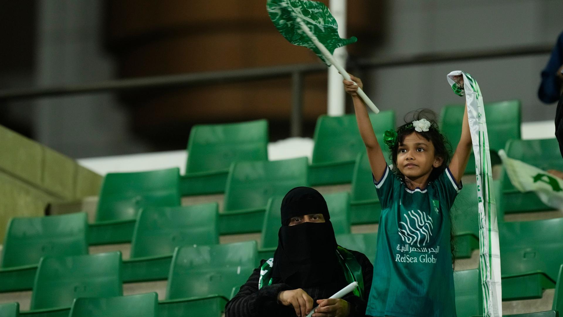 Al-Ahly-Fans jubeln beim Premier-League-Spiel der Frauen zwischen Al Ahli FC und Al Ittihad FC in Jeddah in Saudi-Arabien auf der Tribüne. Ein kleines Mädchen schwenkt dabei eine saudische Fahne. 
