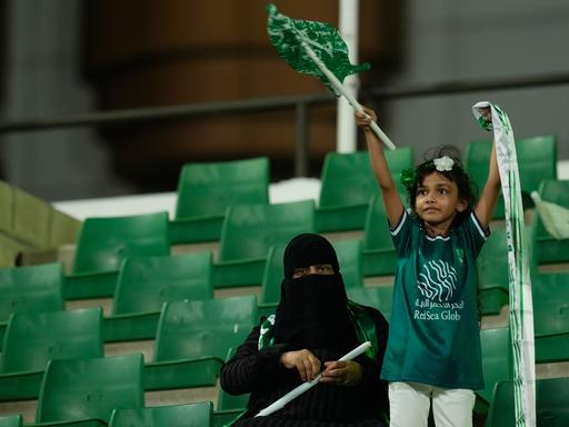 Al-Ahly-Fans jubeln beim Premier-League-Spiel der Frauen zwischen Al Ahli FC und Al Ittihad FC in Jeddah in Saudi-Arabien auf der Tribüne. Ein kleines Mädchen schwenkt dabei eine saudische Fahne. 