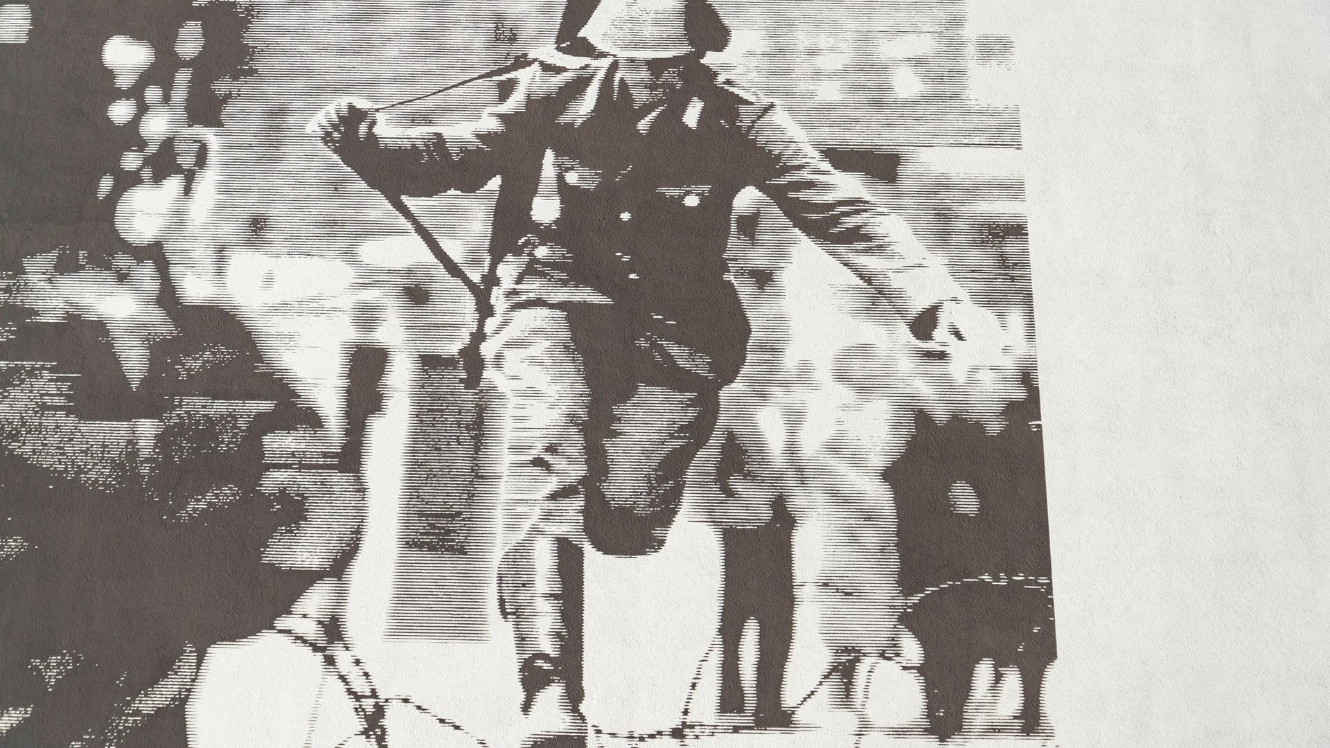 Ein an einem Gebäude aufgeklebtes Foto zeigt, wie ein Soldat im Jahr 1961 über Stacheldraht springt. 