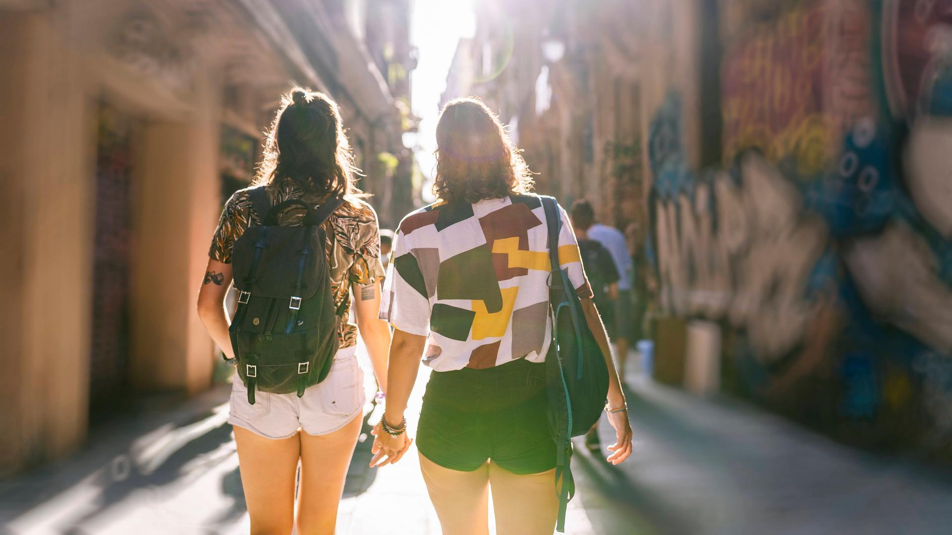Zwei Frauen laufen Hand in Hand durch eine Gasse in einer sommerlichen Altstadt.