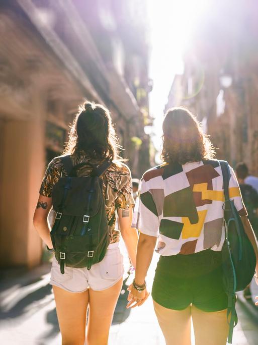 Zwei Frauen laufen Hand in Hand durch eine Gasse in einer sommerlichen Altstadt.