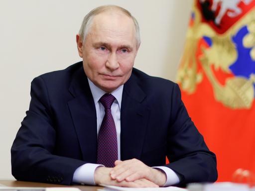Russlands Präsident Wladimir Putin sitzt mit gefalteten Händen an einem Tisch.