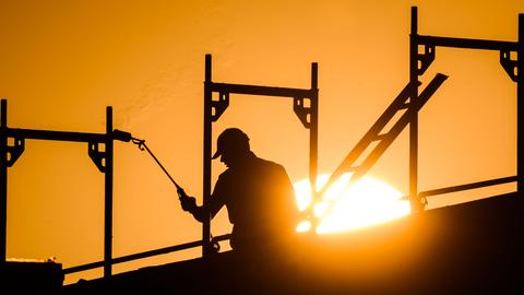 Ein Bauarbeiter steht mit einem Gasbrenner beim Bau eines Mehrfamilienhauses im Neubaugebiet Kronsrode, als am Horizont die Sonne aufgeht. Ein Bauarbeiter steht mit einem Gasbrenner beim Bau eines Mehrfamilienhauses im Neubaugebiet Kronsrode, als am Horizont die Sonne aufgeht.