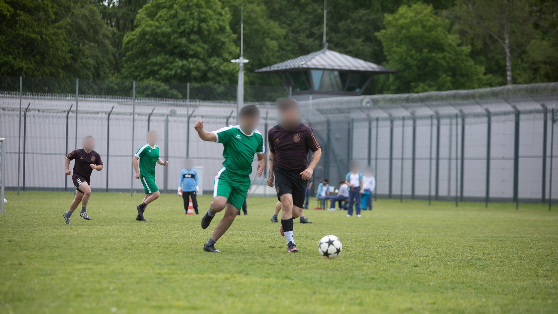 Häftlinge, deren Gesicht aus Gründen des Persönlichkeitsschutzes unkenntlich gemacht worden ist, spielen auf einem von Gefängnismauern umgebenen Bolzplatz Fußball. 