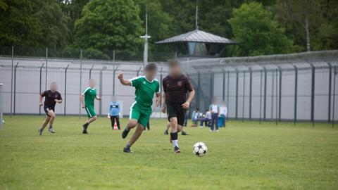 Häftlinge, deren Gesicht aus Gründen des Persönlichkeitsschutzes unkenntlich gemacht worden ist, spielen auf einem von Gefängnismauern umgebenen Bolzplatz Fußball. 