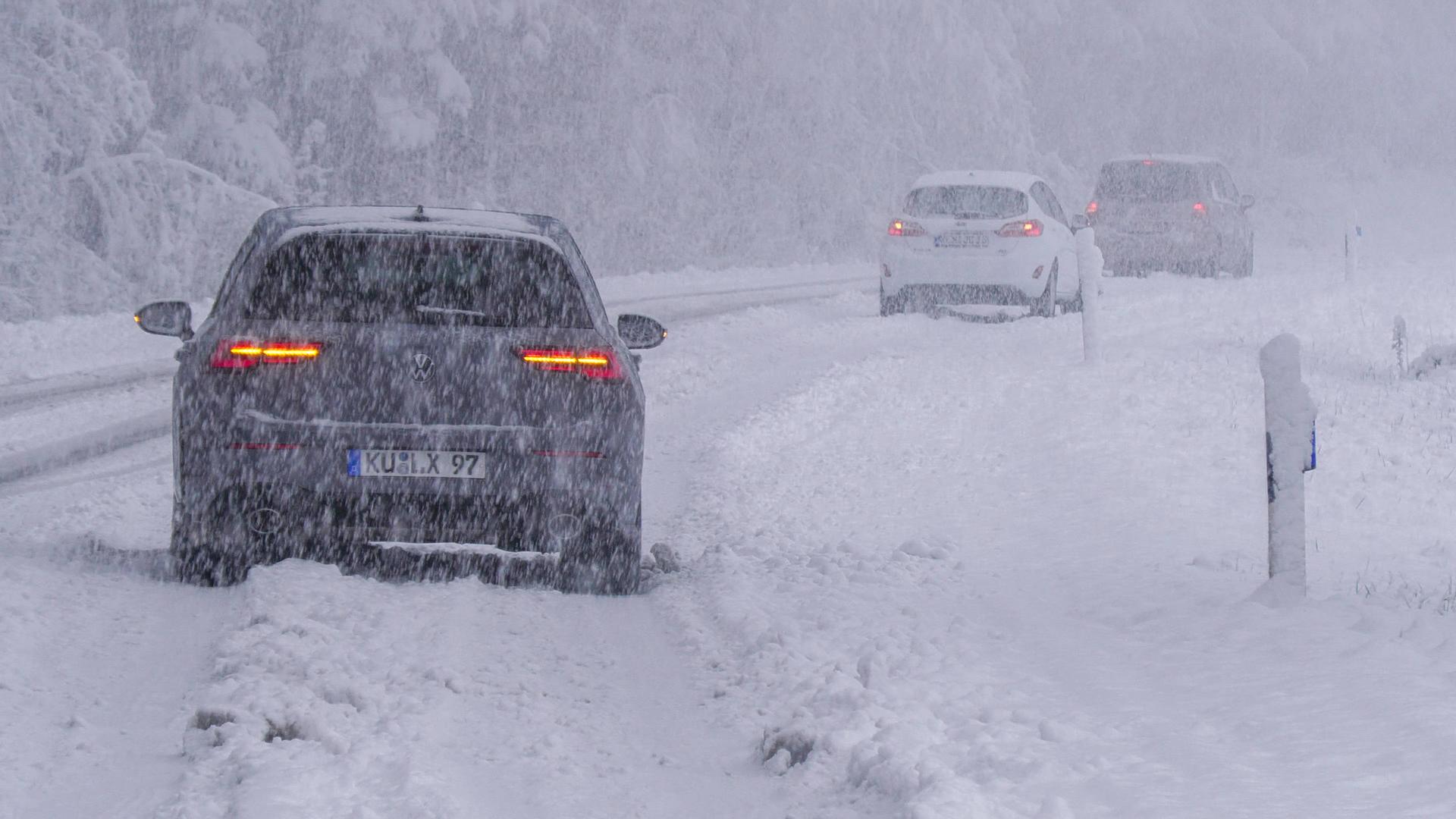 Drei Autos fahren auf einer sehr stark verschneiten Straße.