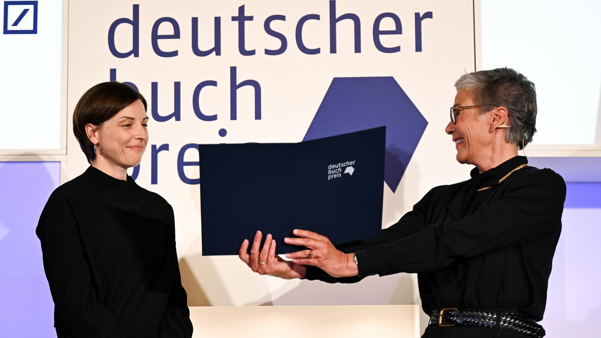 Die Schweizer Autorin Dorothee Elmiger (l) wird von Karin Schmidt-Friderichs, Vorsteherin des Börsenvereins des Deutschen Buchhandels, für ihren Roman "Die Holländerinnen" mit dem Deutschen Buchpreis 2025 ausgezeichnet. Die Schweizer Autorin Dorothee Elmiger (l) wird von Karin Schmidt-Friderichs, Vorsteherin des Börsenvereins des Deutschen Buchhandels, für ihren Roman "Die Holländerinnen" mit dem Deutschen Buchpreis 2025 ausgezeichnet.