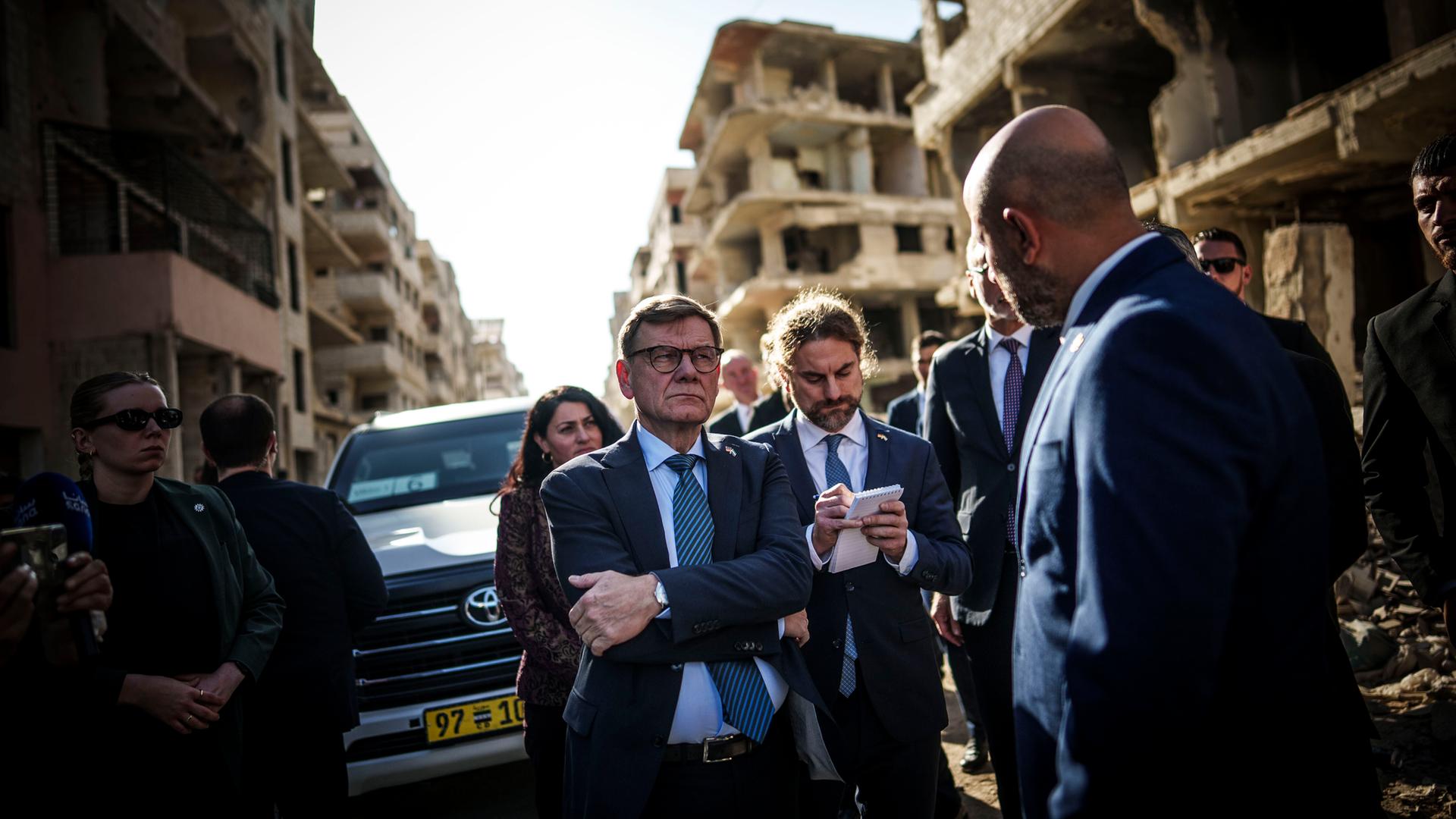 Ein Mann steht vor zerstörten Gebäuden und hört einem Gesprächspartner zu. Ein Mann steht vor zerstörten Gebäuden und hört einem Gesprächspartner zu.