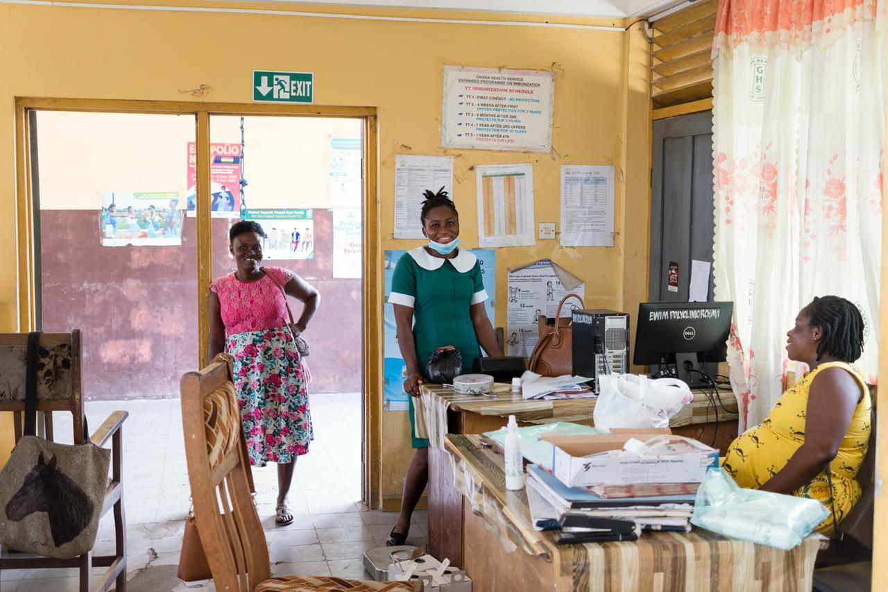 Eine Mitarbeiterin am Schreibtisch und Besucherinnen in der Ewim-Poliklinik in Capecoast, Ghana