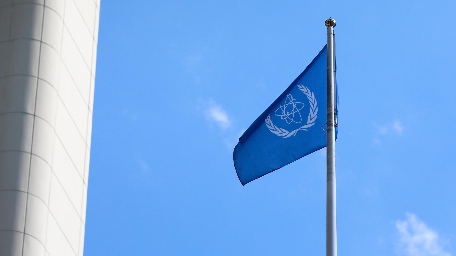 Die Flagge der IAEA vor blauem Himmel. Die Flagge zeigt ein stilisiertes Atom, das von Olivenzweigen umgeben ist. Die Flagge der IAEA vor blauem Himmel. Die Flagge zeigt ein stilisiertes Atom, das von Olivenzweigen umgeben ist.