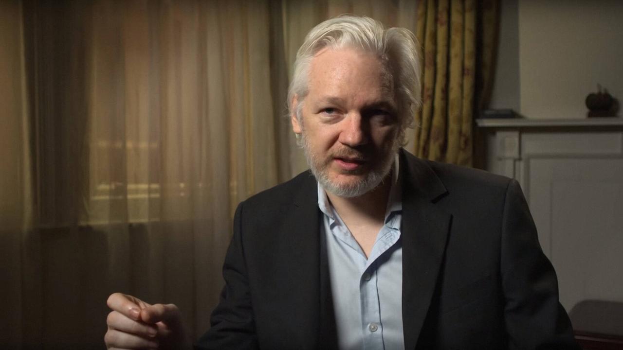 Julian Assange sitzt in einem Zimmer vor einem Fenster mit zugezogenen Vorhängen