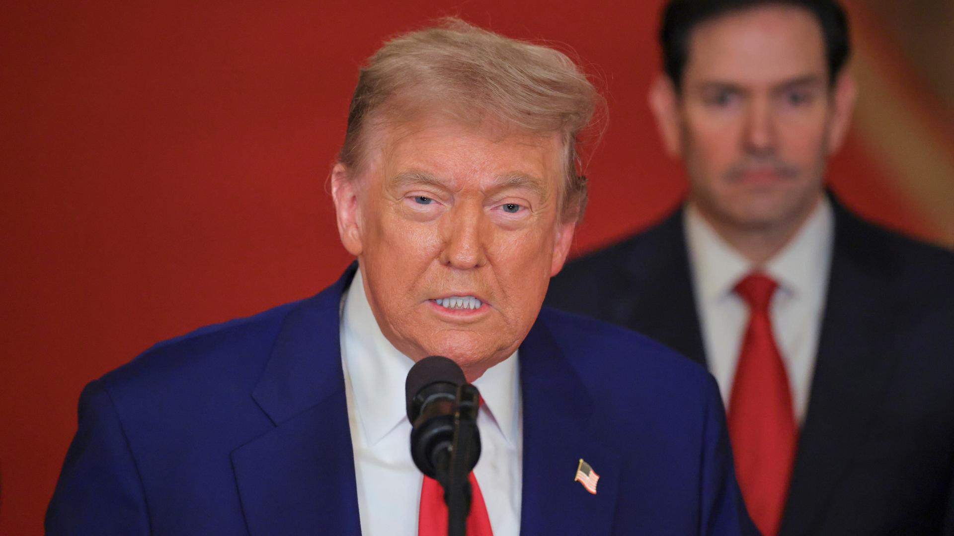 US-Präsident Trump spricht in ein Mikrofon. Im Hintergrund steht US-Außenminister Rubio. US-Präsident Trump spricht in ein Mikrofon. Im Hintergrund steht US-Außenminister Rubio.