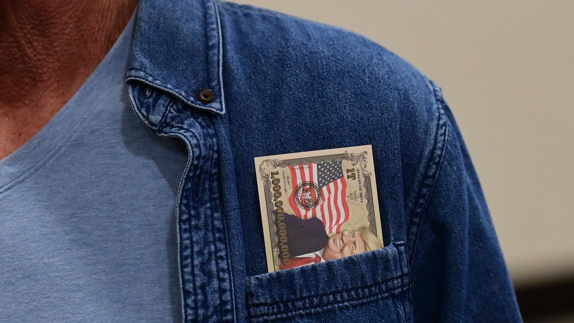 Ein Mann trägt in der Tasche einer Jeansjacke während einer Kundgebung für den republikanischen Kandidaten für das Amt des Gouverneurs von Pennsylvania, Doug Mastriano, einen gefälschten Geldschein, auf dem der ehemalige Präsident Donald Trump abgebildet ist. 