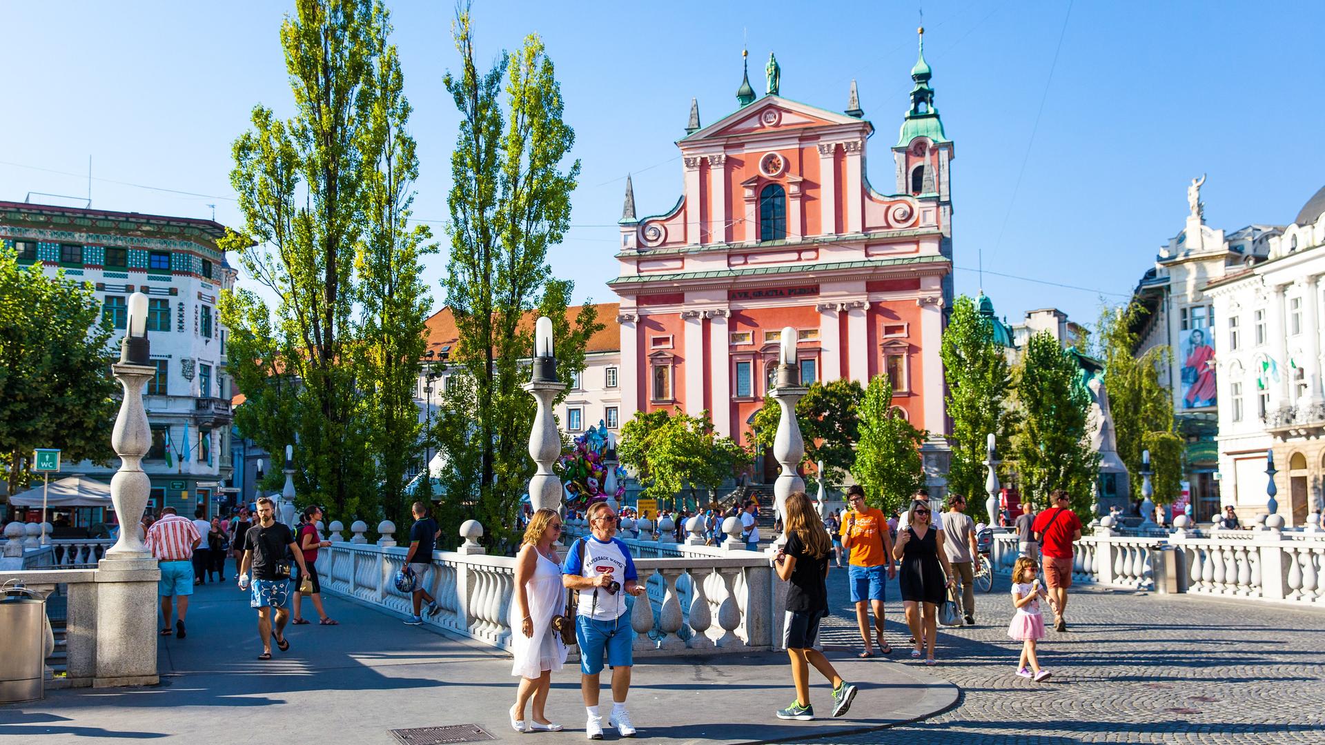 Der Preseren-Platz, die Fußgängerzone in der Hauptstadt Ljubljana mit den drei Brücken (Tromostovje) und vielen Menschen und der rosa Franziskanerkirche.