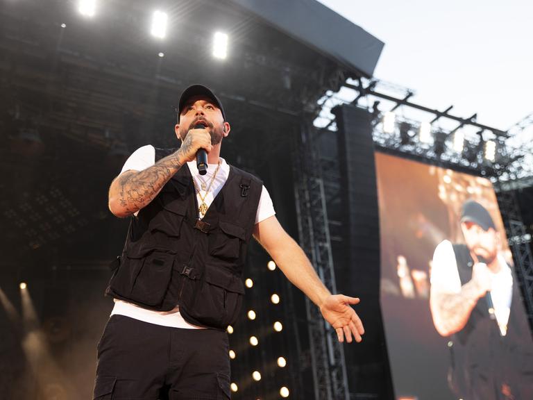 Christopher Seiler steht mit dem Mikro in der Hand auf einer großen Bühne im Ernst-Happel-Stadion in Wien und singt. 