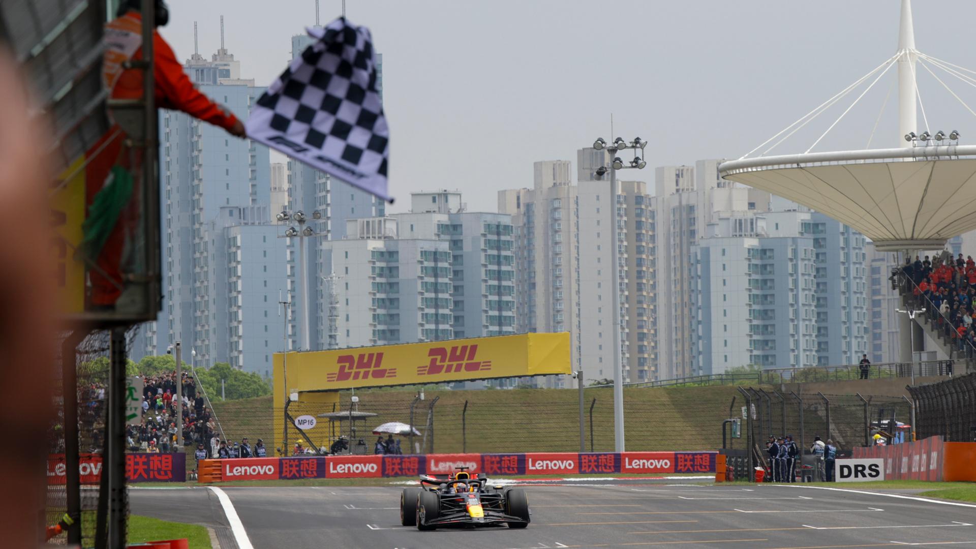 Max Verstappen fährt im Red Bull über die Ziellinie. Im Hintergrund sind Hochhäuser zu sehen.