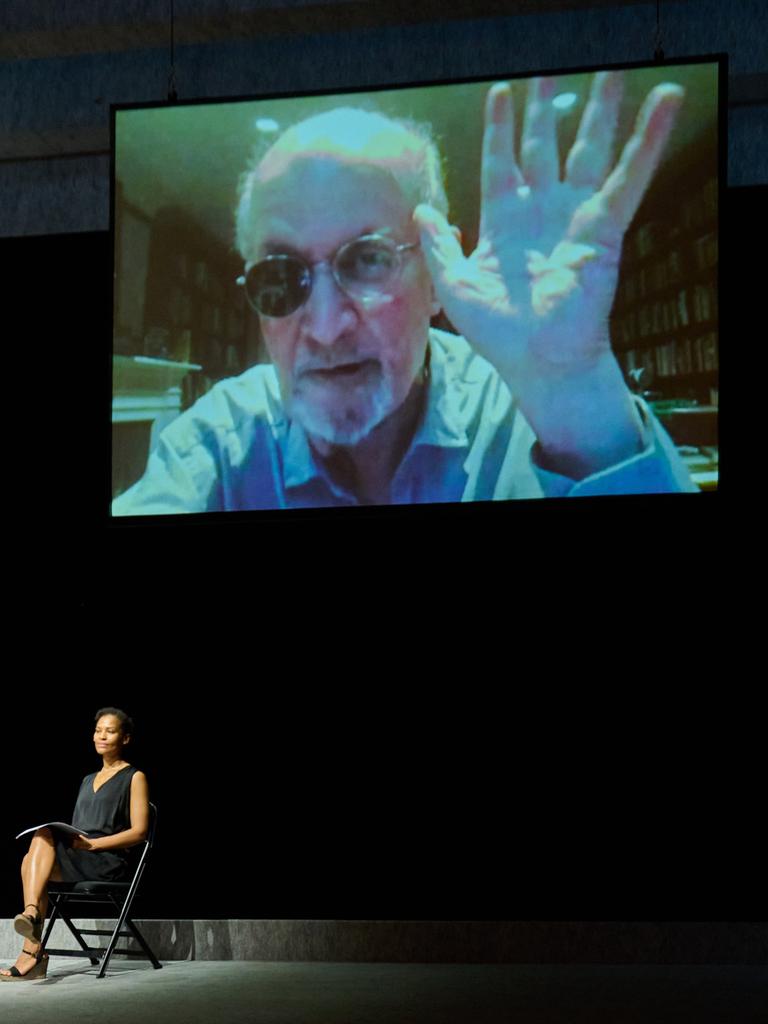 Schriftsteller Salman Rushdie zeigt, live aus New York zugeschaltet, seine bei einem Anschlag verletzte und inzwischen genesene Hand, während der Übersetzer Bernhard Robben, Schriftsteller Daniel Kehlmann und Schauspielerin Cynthia Micas der Bühne sitzen. 