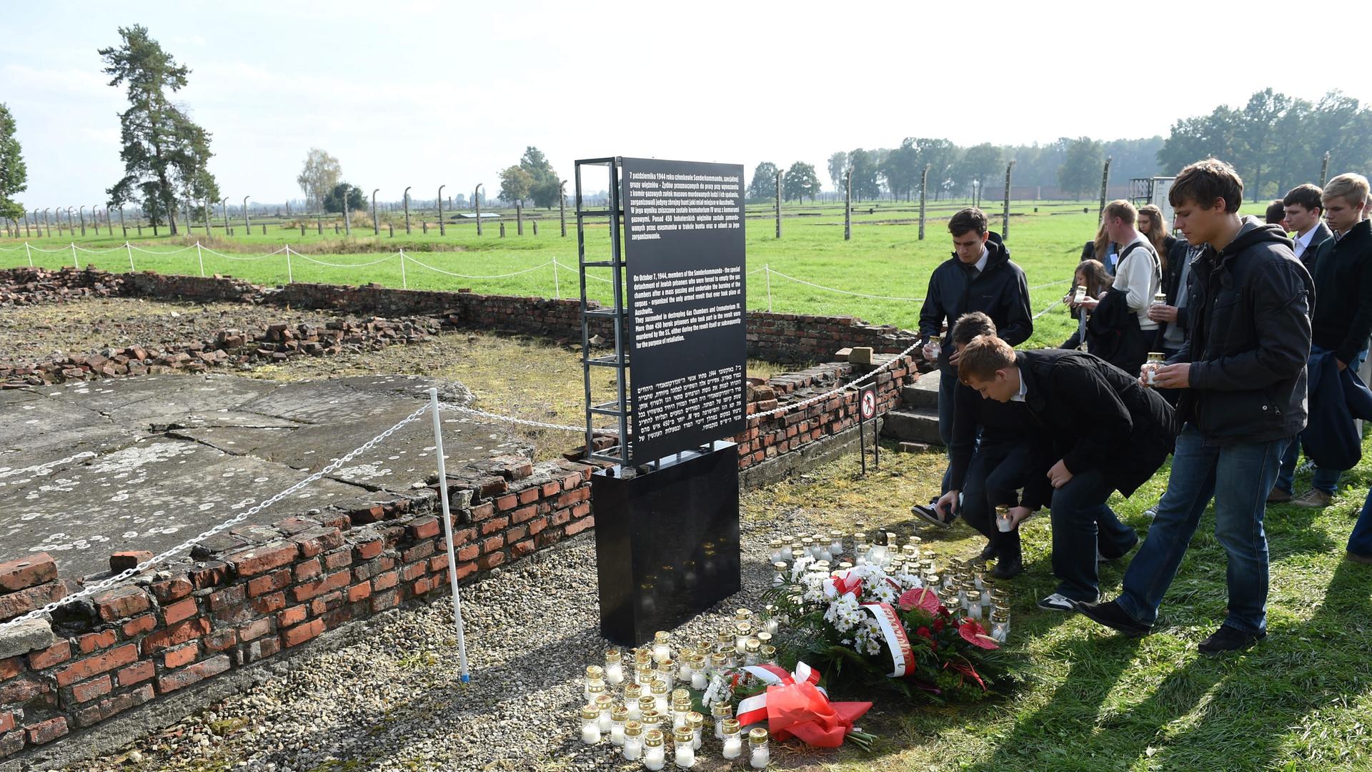 Menschen legen vor einer Gedenktafel im KZ Auschwitz-Birkenau zur Erinnerung an den Aufstand des Sonderkommandos Blumen ab.