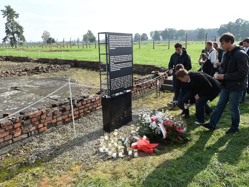 Menschen legen vor einer Gedenktafel im KZ Auschwitz-Birkenau zur Erinnerung an den Aufstand des Sonderkommandos Blumen ab.