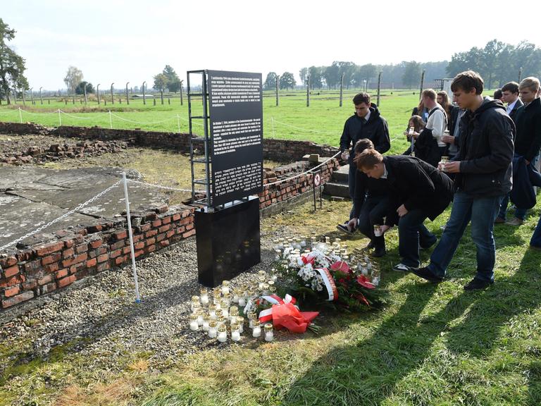 Menschen legen vor einer Gedenktafel im KZ Auschwitz-Birkenau zur Erinnerung an den Aufstand des Sonderkommandos Blumen ab. (Quelle: Picture Alliance)