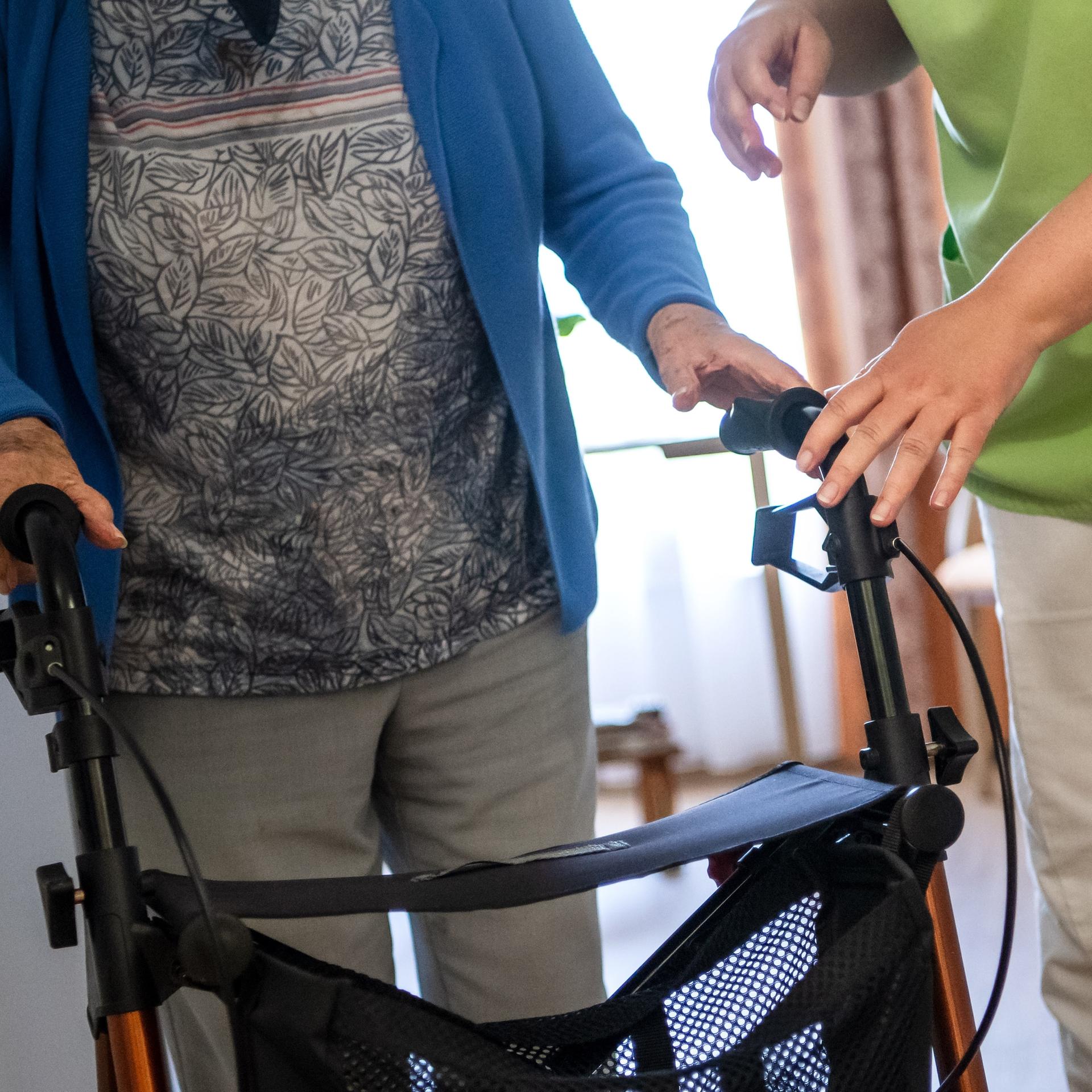 Eine Pflegefachkraft hilft einer Bewohnerin eines Seniorenheims mit ihrem Rollator.