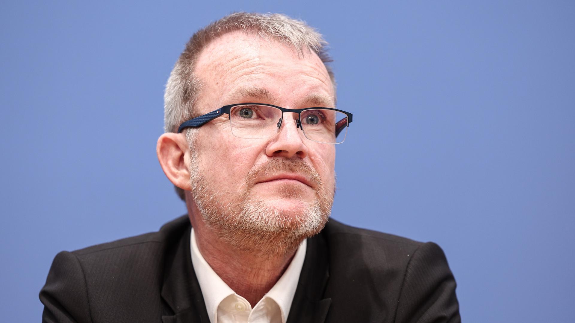 Jens Baas, Vorstandsvorsitzender der Techniker Krankenkasse, nimmt an einer Pressekonferenz teil. Er sitzt vor blauem Hintergrund.