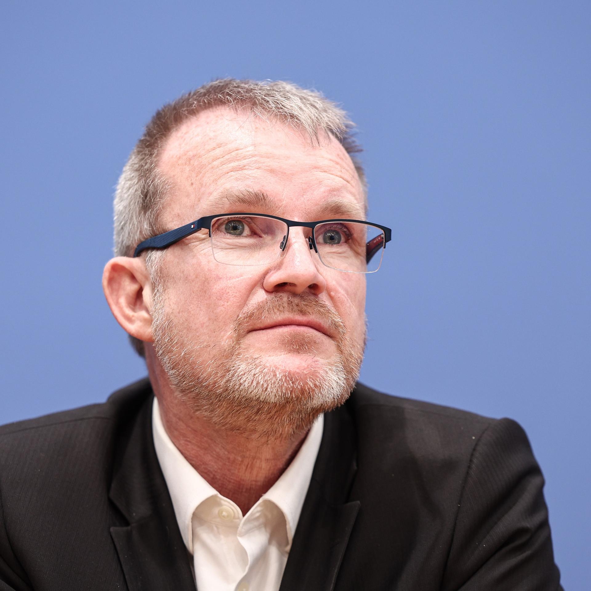 Jens Baas, Vorstandsvorsitzender der Techniker Krankenkasse, nimmt an einer Pressekonferenz teil. Er sitzt vor blauem Hintergrund.