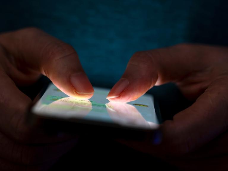 Eine Frau tippt auf ihrem Telefon. Die Beleuchtung hebt die Finger des Benutzers und den Bildschirm des Smartphones hervor. Eine Frau tippt auf ihrem Telefon. Die Beleuchtung hebt die Finger des Benutzers und den Bildschirm des Smartphones hervor.