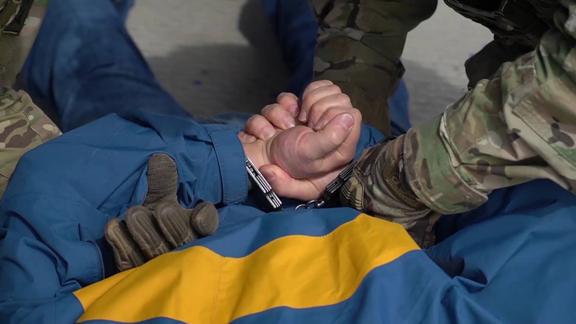 Ein Körper, der auf dem Rücken liegt, bekommt Handschellen von einer Person in einem Camouflage-Anzug angelegt