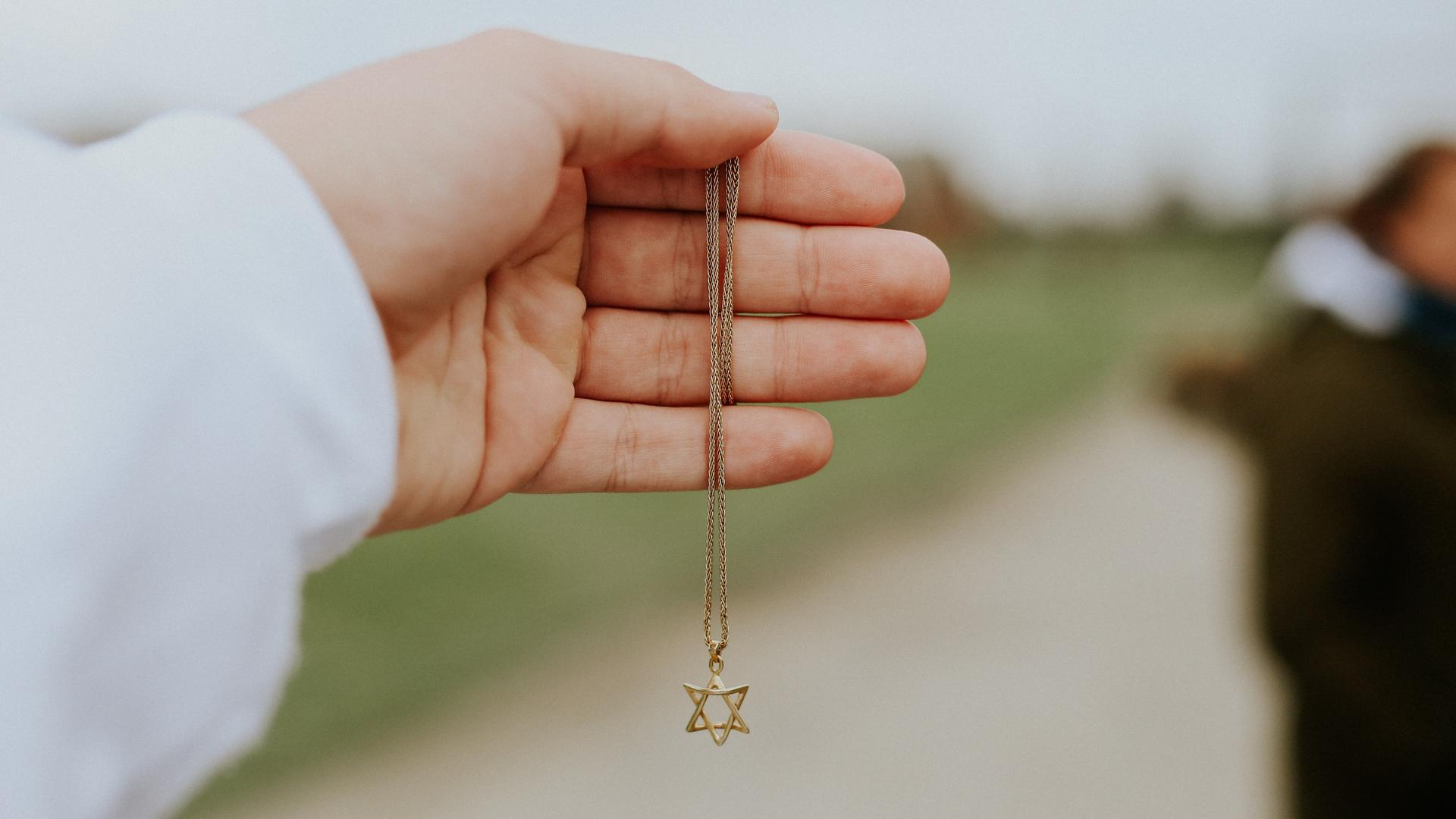 Nahaufnahme einer Hand, die eine goldene Halskette mit einem Anhänger in Form eines Davidsterns hält.