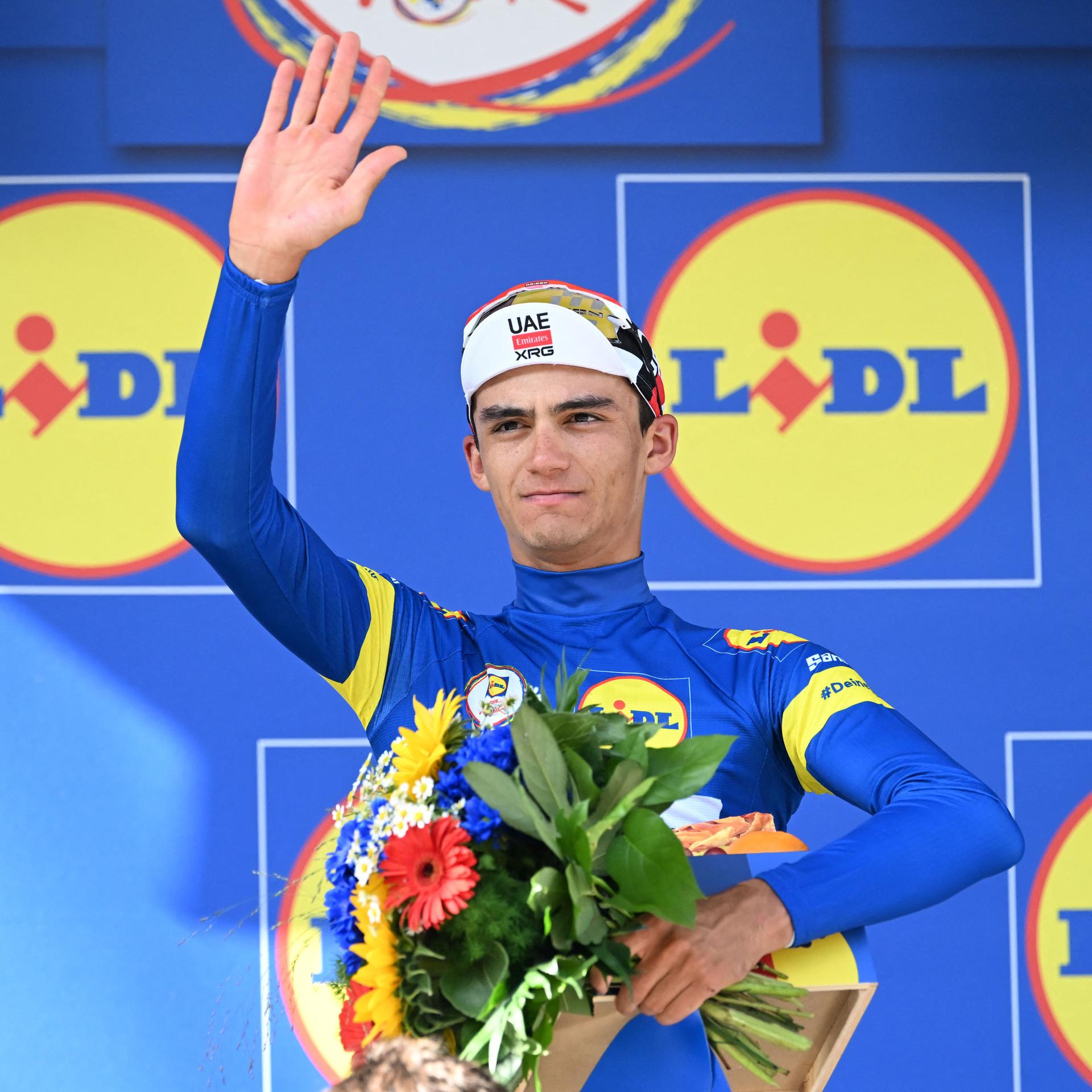 Radsport: Deutschland Tour - Der Mexikaner Isaac del Toro bejubelt seinen Gesamtsieg. Er hält einen Blumenstrauß in der einen Hand und winkt mit der anderen.