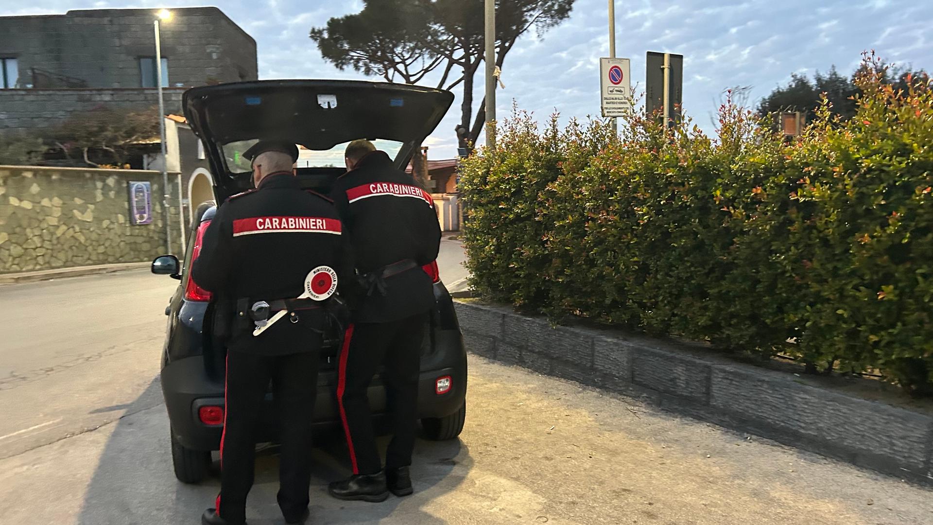 Zwei Beamte der italienischen Carabinieri stehen hiner ihrem Auto. Der Kofferraum ist geöffnet. 