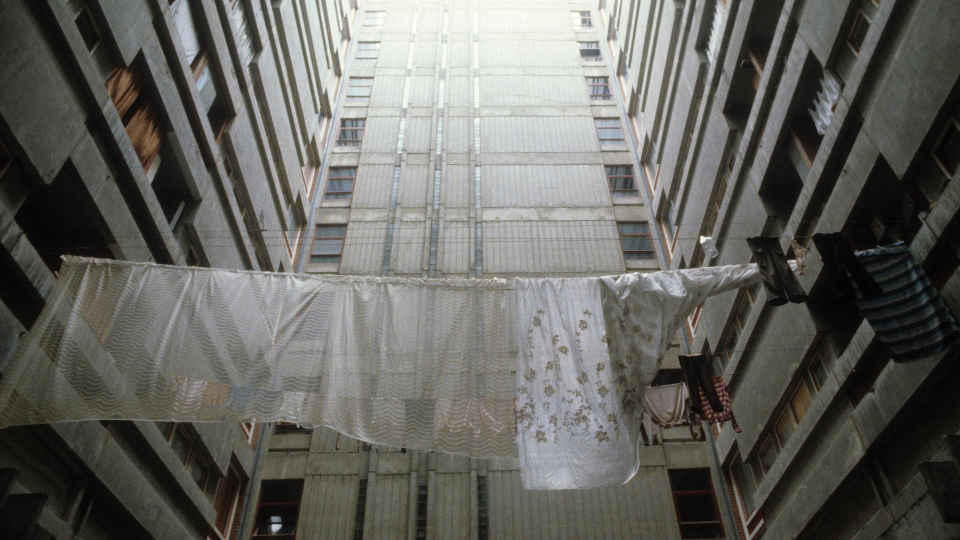 Historische analoge Farbfotografie: Wäsche hängt zum Trocknen auf der Leine zwischen Plattenbautfassaden im Belgrad Ende der 80er Jahre. Es ist kein Horizont zu sehen, aber es scheint ein fahles Licht von oben auf den Beton 