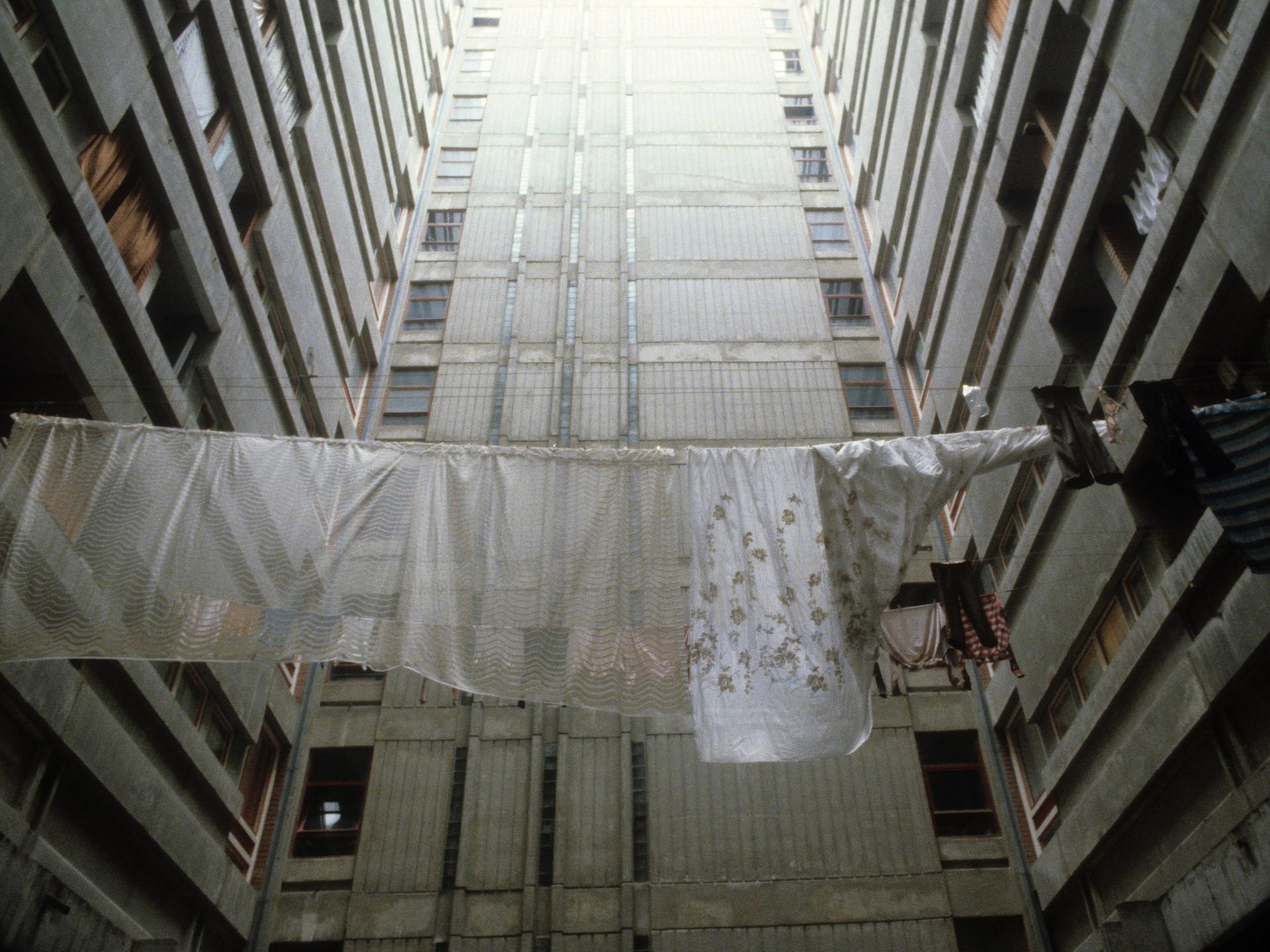 Historische analoge Farbfotografie: Wäsche hängt zum Trocknen auf der Leine zwischen Plattenbautfassaden im Belgrad Ende der 80er Jahre. Es ist kein Horizont zu sehen, aber es scheint ein fahles Licht von oben auf den Beton 