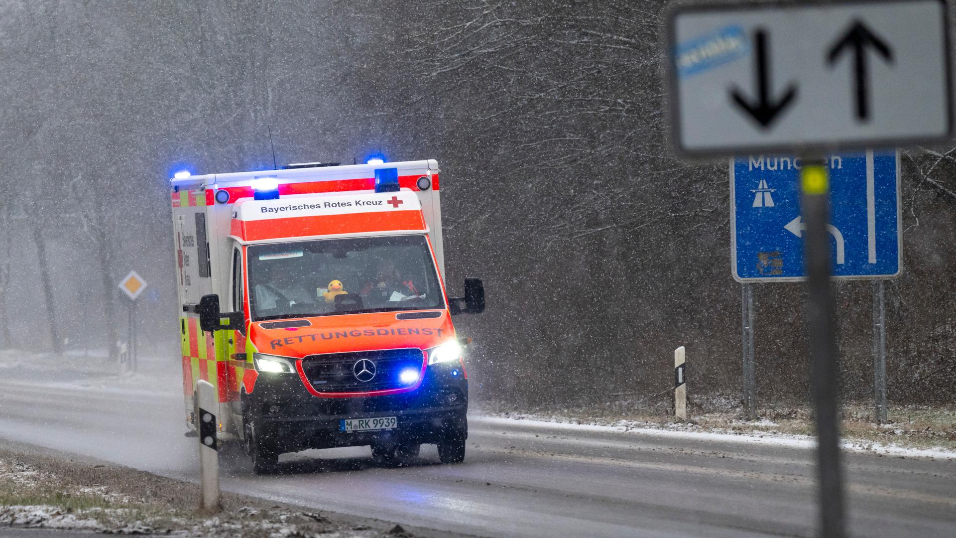 Ein Rettungswagen fährt bei winterlichem Wetter mit Blaulicht auf einer Straße. 