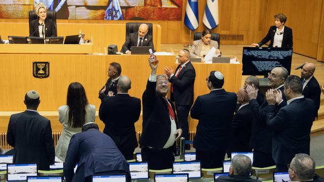 Minister Ben-Gvir steht im israelischen Parlament. Er hält eine Flasche Sekt in die Höhe. Neben ihm stehen mehrere Abgeordnete und klatschen.