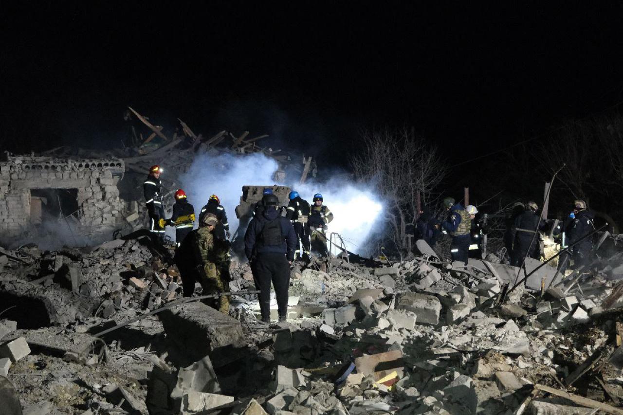 Dutzende Rettungskräfte stehen bei Nacht in den Trümmern eines zerstörten Hauses. 