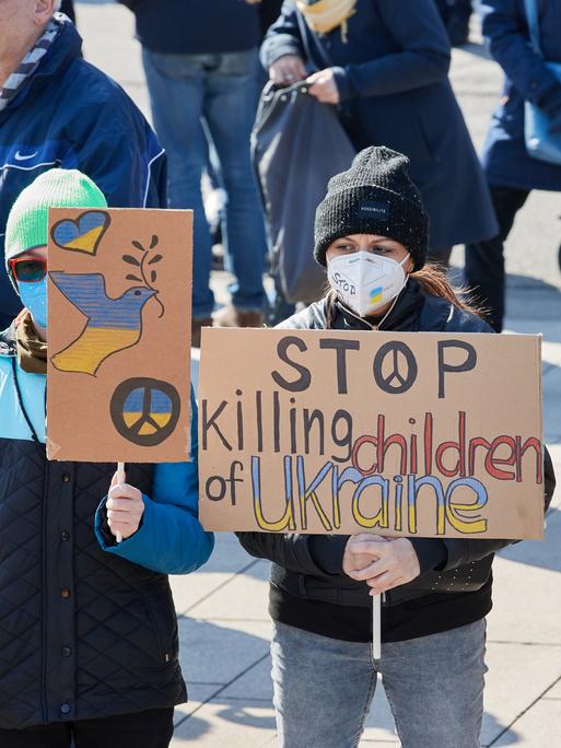 Teilnehmende einer Demonstration für Frieden in der Ukraine und Sicherheit in Europa halten in Hamburg Transparente mit der Aufschrift "Stop killing children of Ukraine" und "Stop war now".