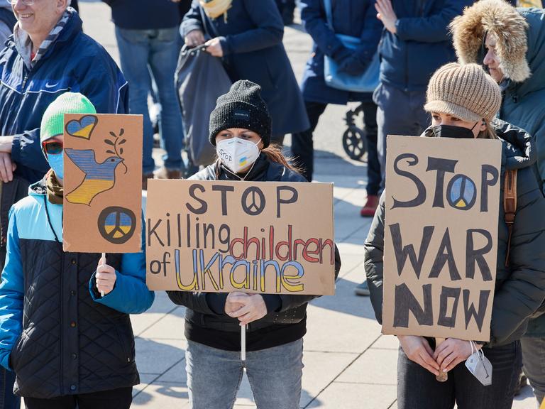 Teilnehmende einer Demonstration für Frieden in der Ukraine und Sicherheit in Europa halten in Hamburg Transparente mit der Aufschrift "Stop killing children of Ukraine" und "Stop war now".