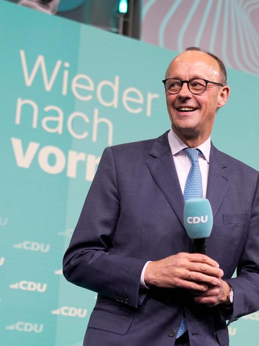 CDU-Chef Friedrich Merz freut sich am Wahlabend. Hinter ihm eine Deutschlandkarte und der Slogan "Wieder nach vorn".  Er hält ein Mikro mit CDU in der Hand. 