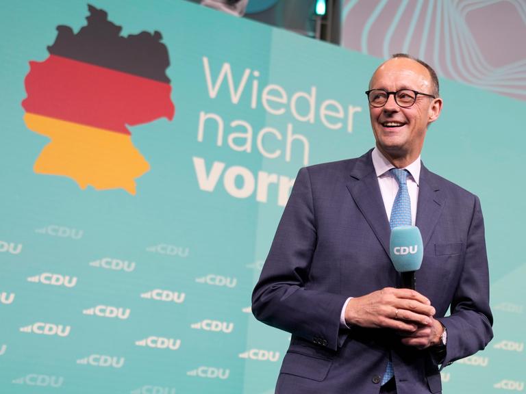 CDU-Chef Friedrich Merz freut sich am Wahlabend. Hinter ihm eine Deutschlandkarte und der Slogan "Wieder nach vorn".  Er hält ein Mikro mit CDU in der Hand. 