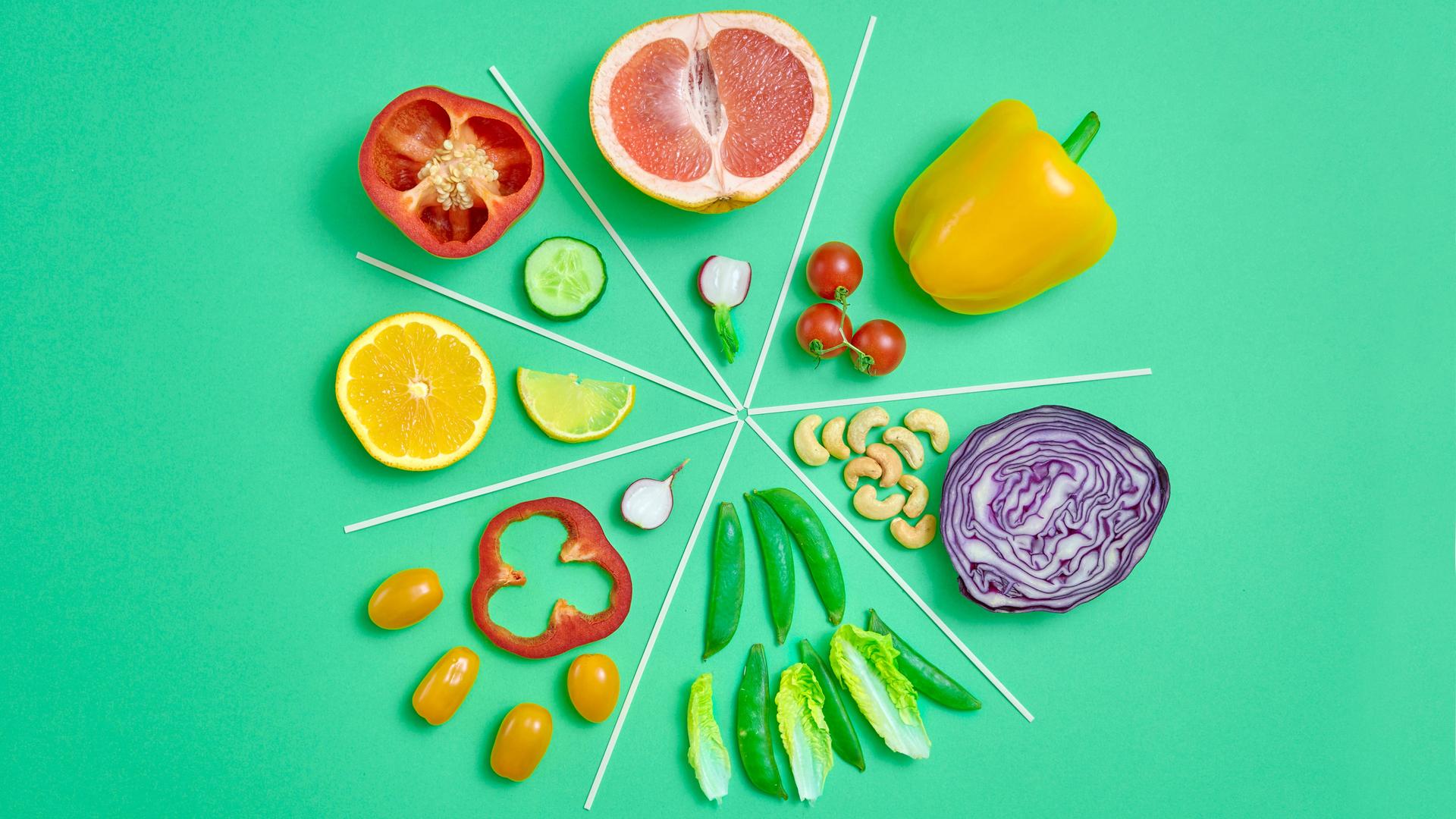 Infografisches Kreisdiagramm aus geschnittenem Gemüse und Obst auf grünem Hintergrund.