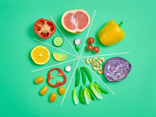 Infografisches Kreisdiagramm aus geschnittenem Gemüse und Obst auf grünem Hintergrund.