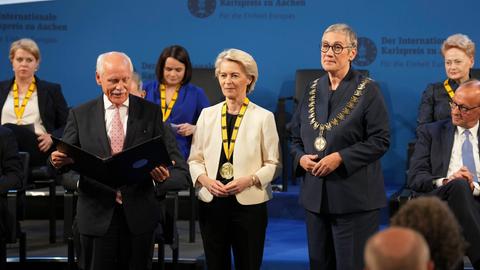Ursula von der Leyen ist der Karlspreis verliehen worden. Sie steht zwischen anderen Menschen bei der Verleihung. Die Karls-Preis-Medaille hängt um ihren Hals. 