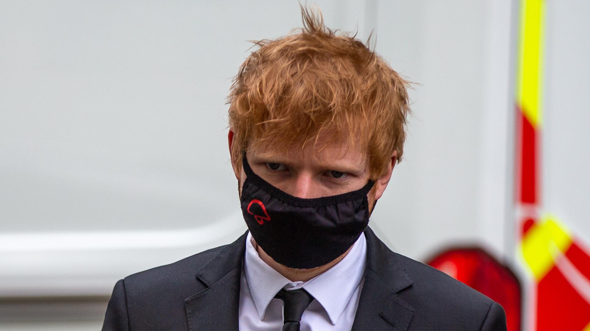 Musiker Ed Sheeran erscheint in Anzug und Krawatte, mit einer Schutzmaske im Gesicht, vor Gericht. Der Musiker hat rote, strubbelige Haare.