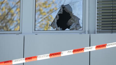 Das Bild zeigt ein zersplittertes Fenster mit einem Loch. Davor rot-weißes Absperrband mit der Aufschrift "Polizeiabsperrung"