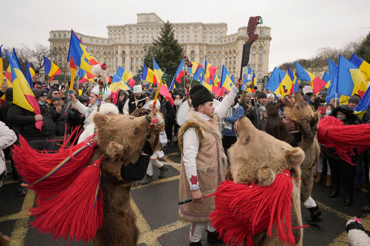 Rumänien, Bukarest: Demonstranten, die gegen die Einführung des grünen Covid-19-Zertifikats protestieren, versammeln sich vor dem Parlamentspalast und werden von einer Gruppe von Menschen begleitet, die Bärenfelle tragen und Neujahrsrituale durchfühen.